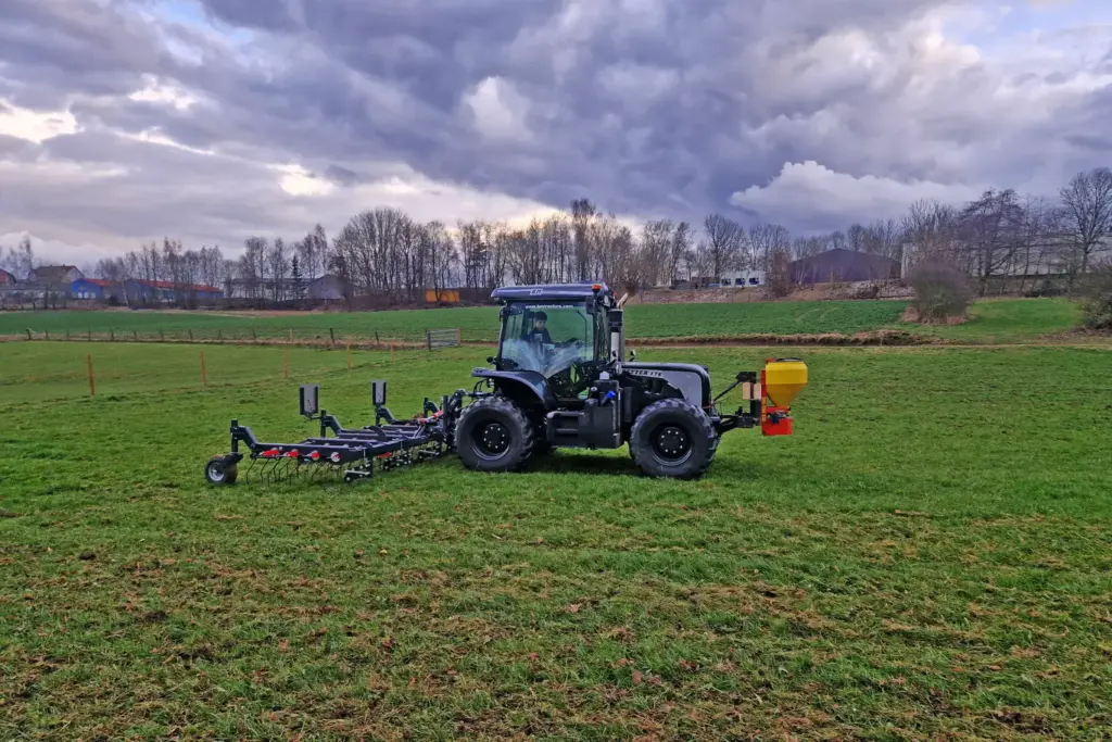 Blauer Traktor auf Weideland beim Grünlandstriegel