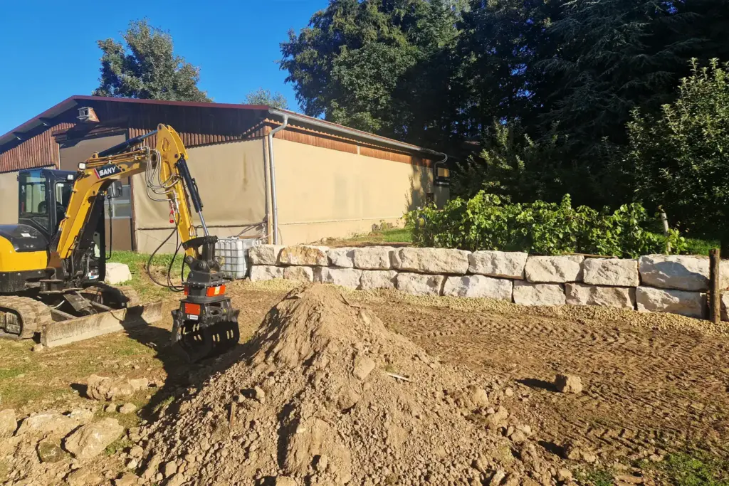 Fotografie einer Baustelle mit Natursteinmauer und Bagger im Sommer
