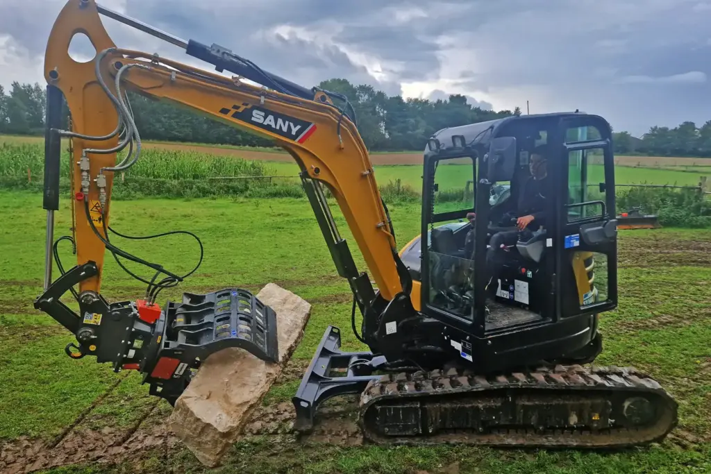 Ein Raupenfahrzeug transportiert Natursteine für den Bau einer Mauer.