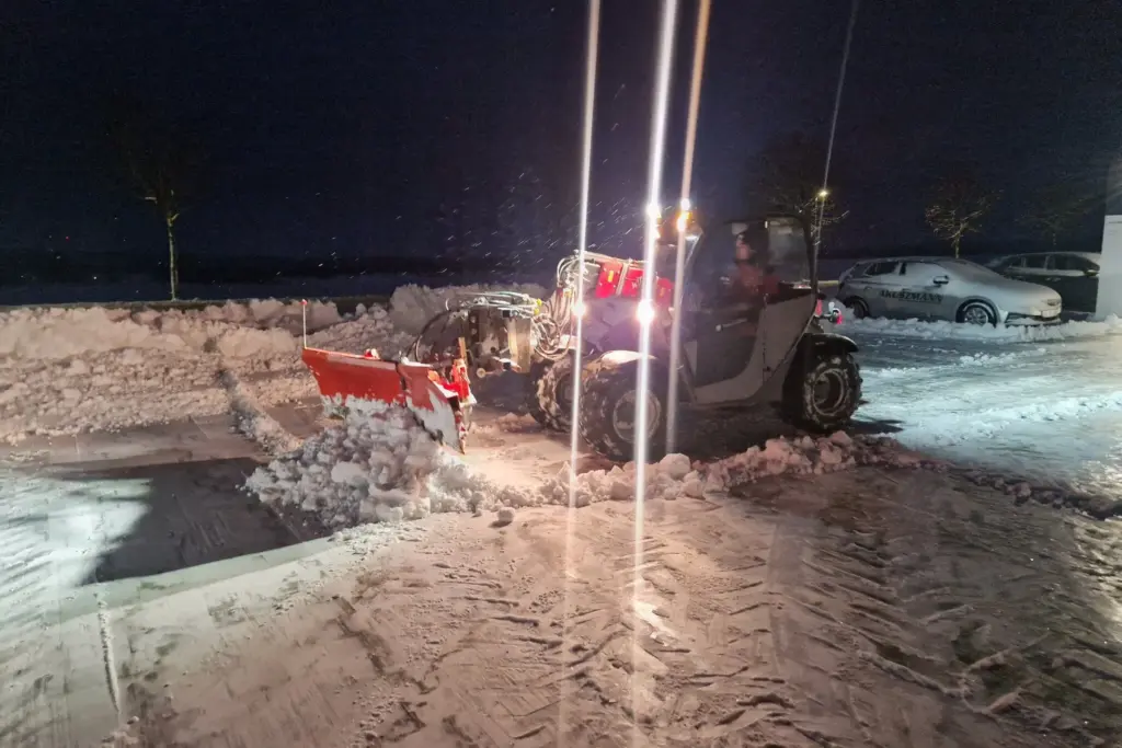 Kleiner grüner Bagger beim Räumen von Schnee auf der Straße