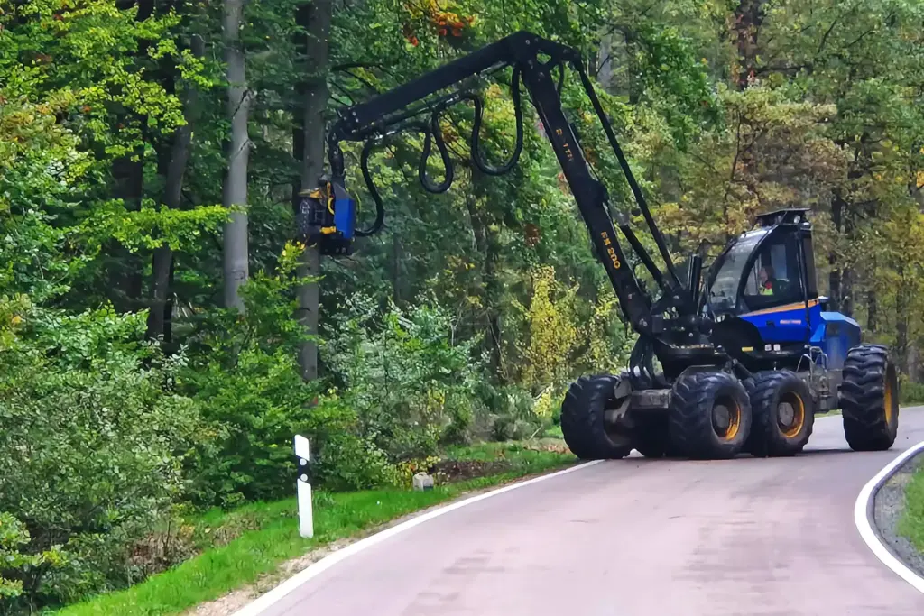 Ein blauer Harvester bei der Fällung eines Baumes auf einer Landstraße am Waldrand