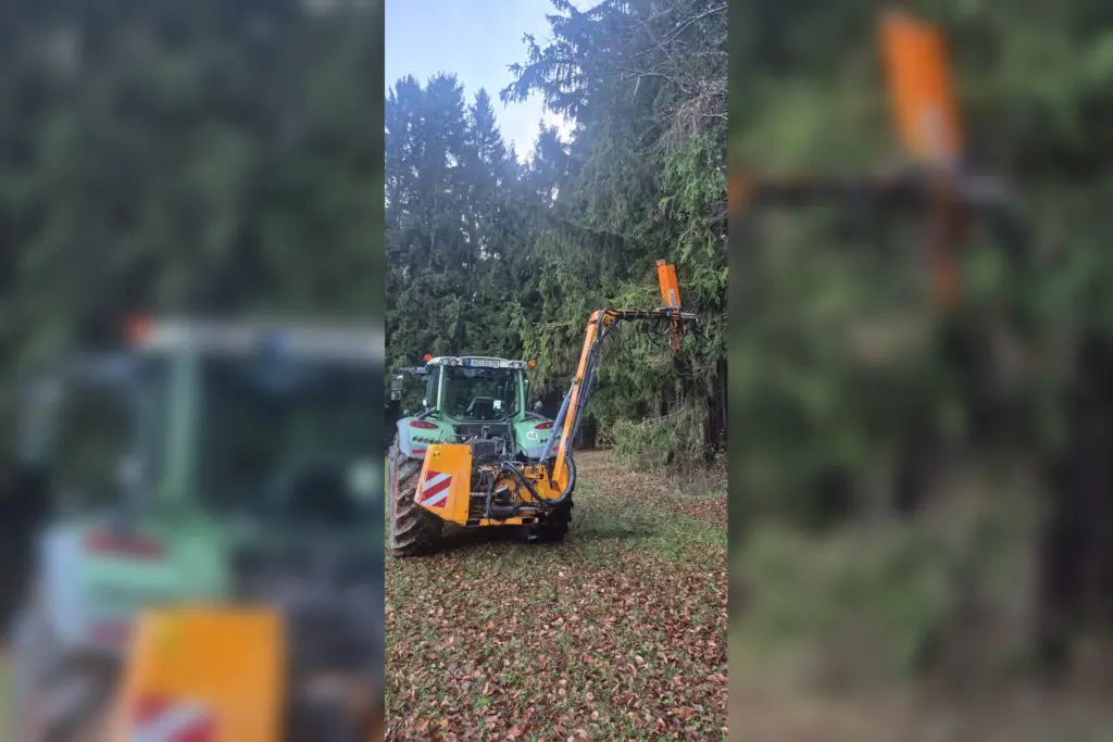 Traktor mit Ausleger beim Lichtraumschnitt an einem bewaldeten Weg