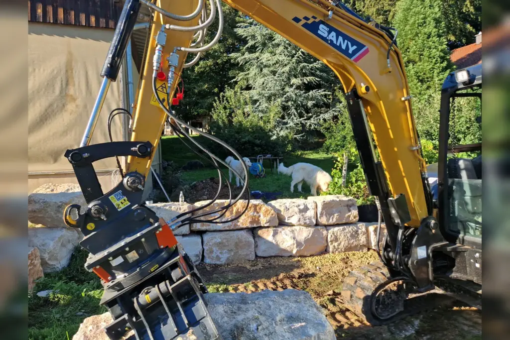 Bagger mit Greifer beim Bau einer Natursteinmauer
