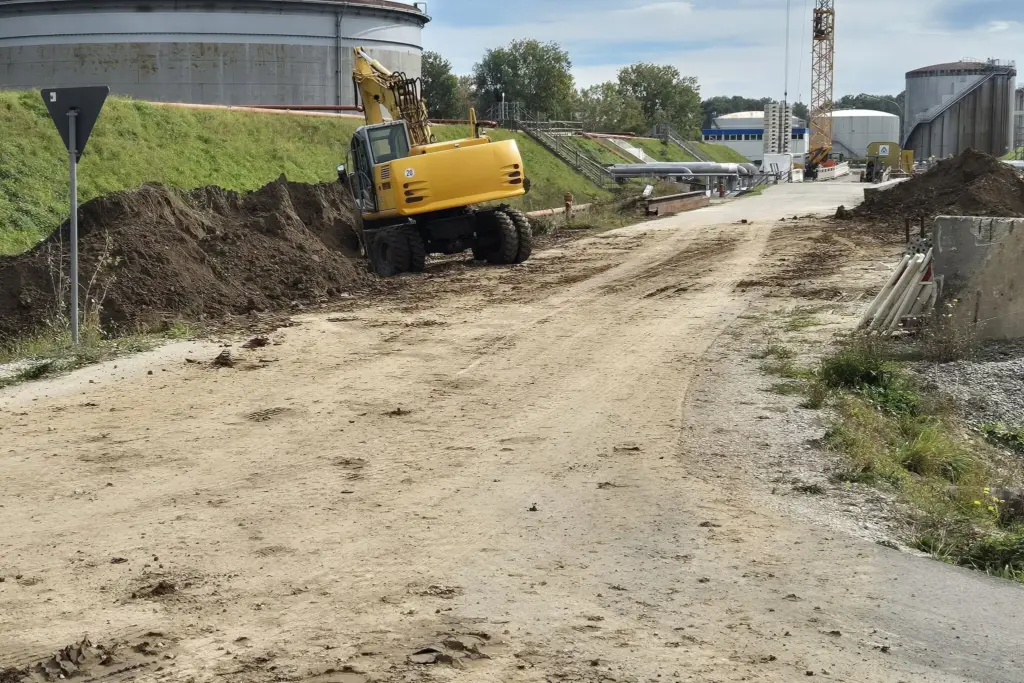 Ein lange Einfahrt wird vorbereitet für Pflasterbauarbeiten. Es sind mehrere Fahrzeuge für den Bau zu sehen, während die Auffahrt noch voll Schotter ist.
