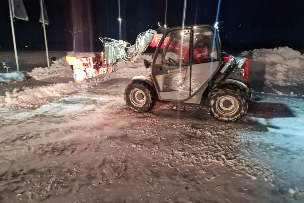 Kleiner grüner Bagger auf einer verschneiten Straße beim Winterdienst